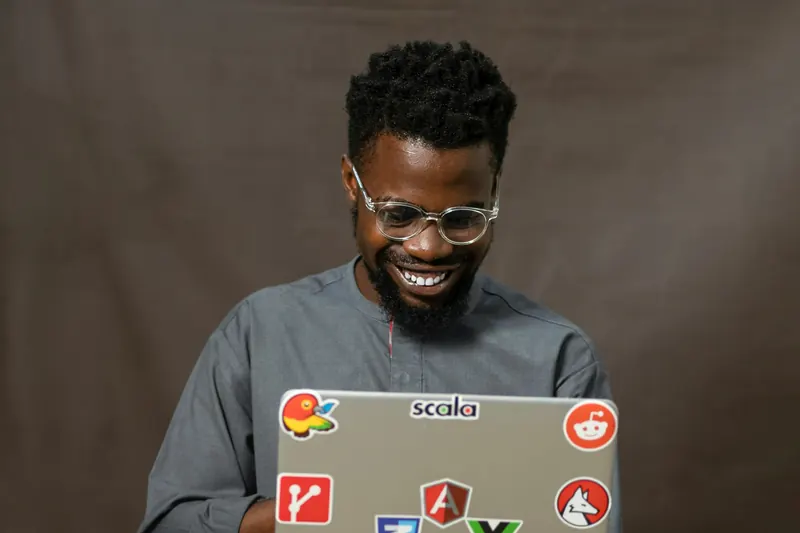 A smiling developer holding a laptop covered in tech stickers