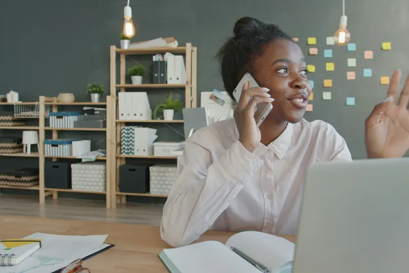 A woman on a phone call at her desk, waving hello