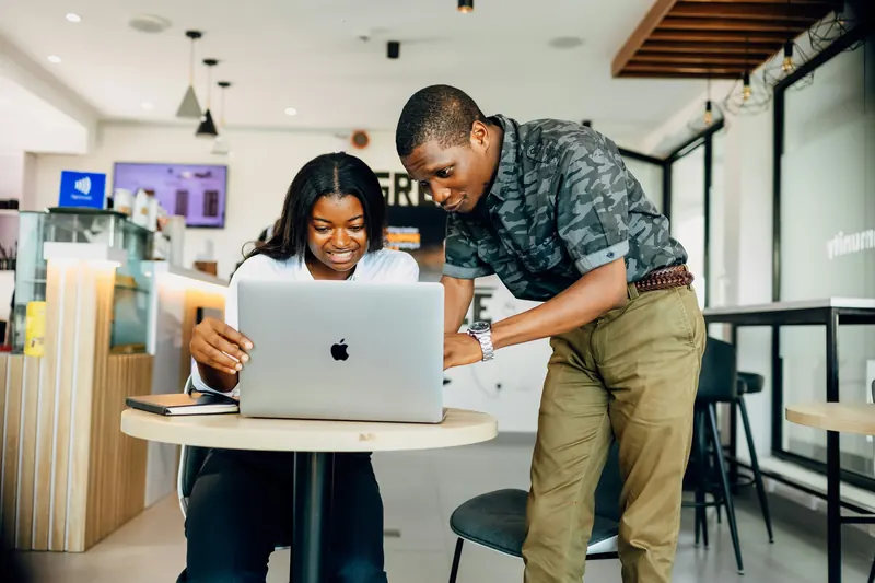 A developer leans over to help a colleague at her laptop